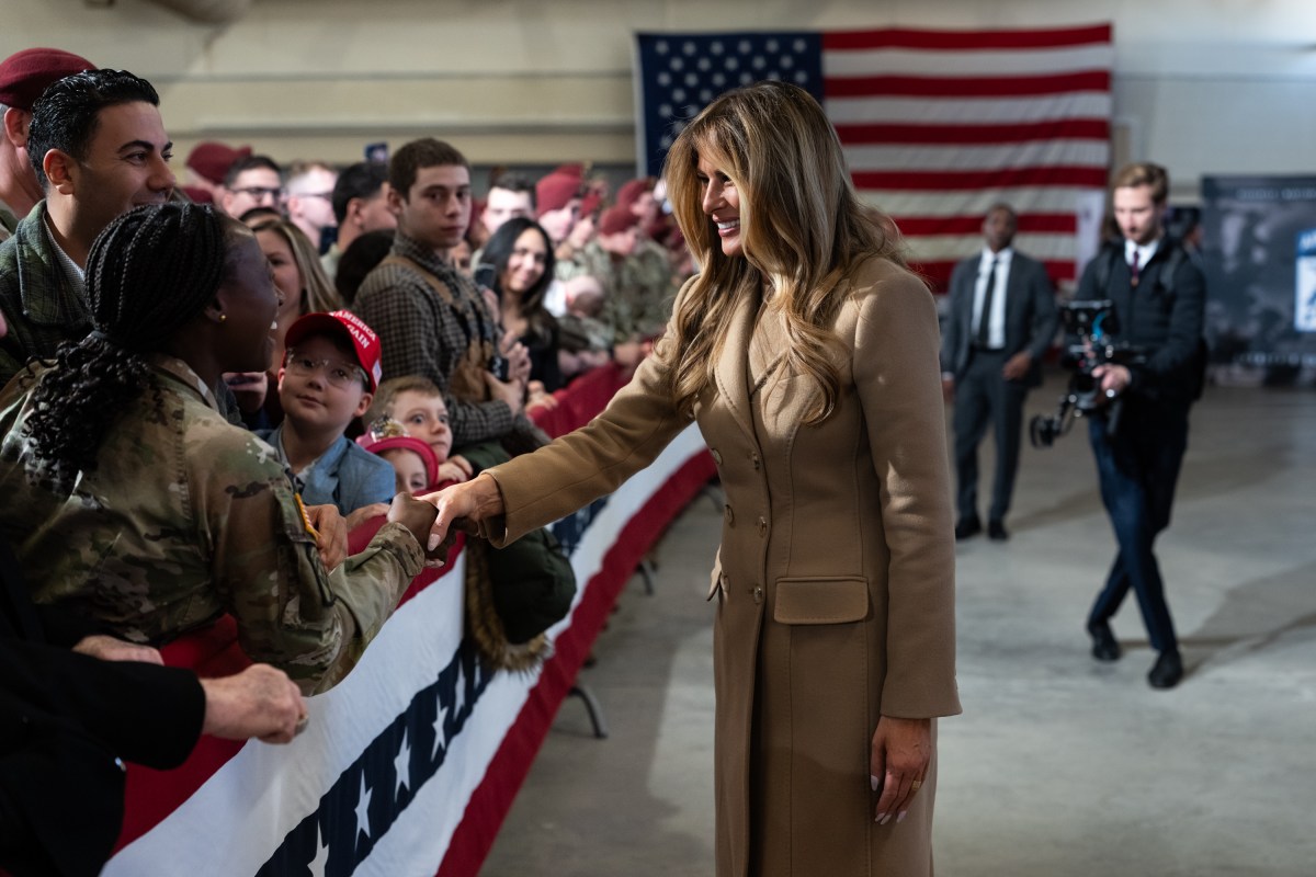 First lady Melania Trump shakes hands with a uniformed service member as military families stand behind a red, white and blue barrier at Fort Bragg.